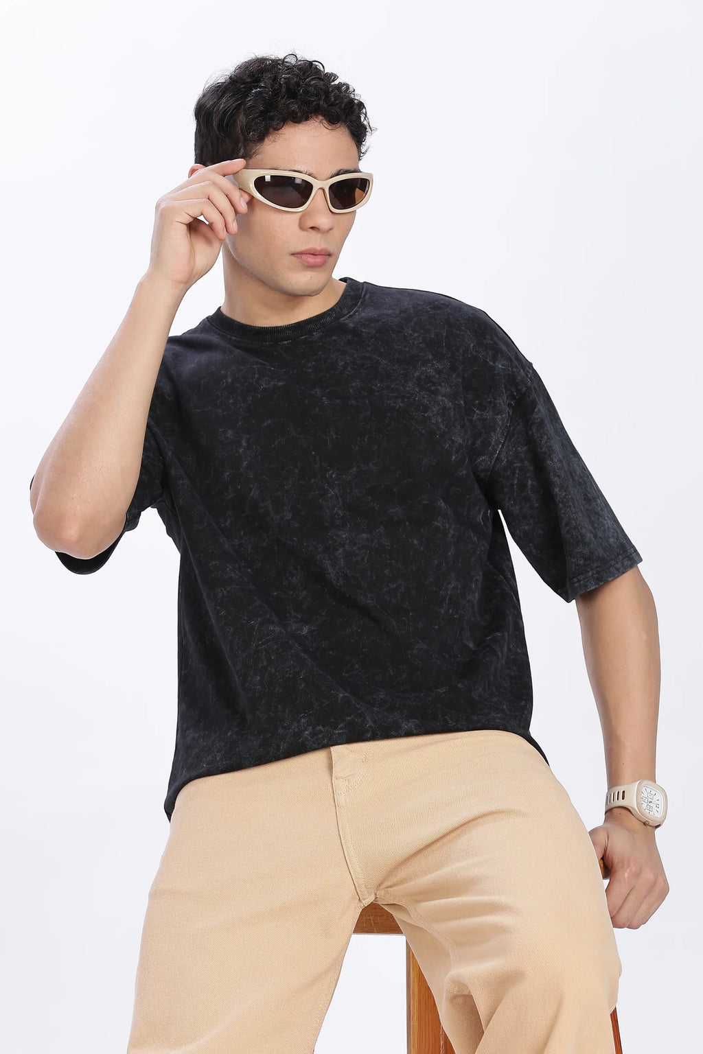 Man wearing a black textured shirt and beige pants with sunglasses on a white background