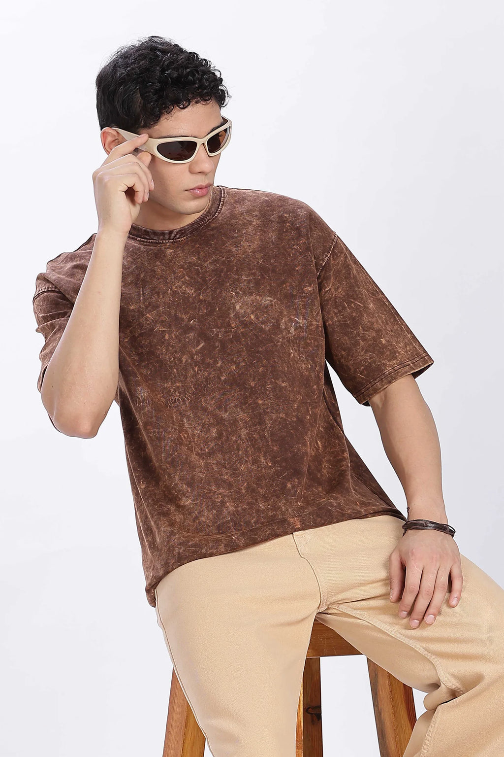 Person wearing a brown acid-wash t-shirt and beige pants, sitting on a white background.