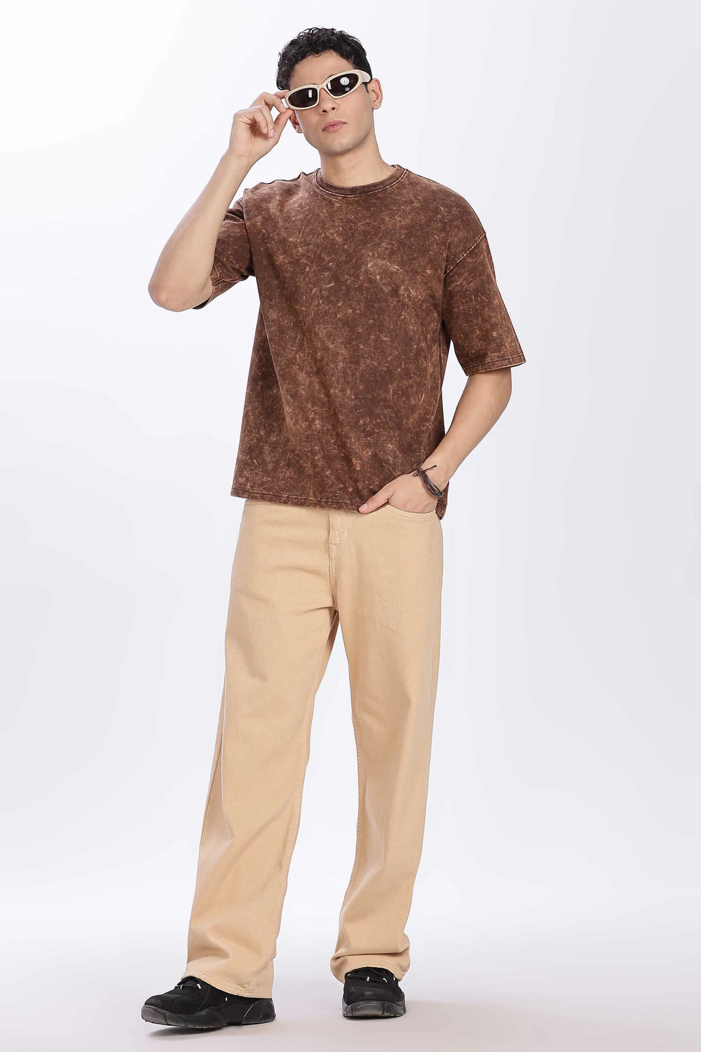 Man wearing a brown patterned shirt and beige pants on a white background