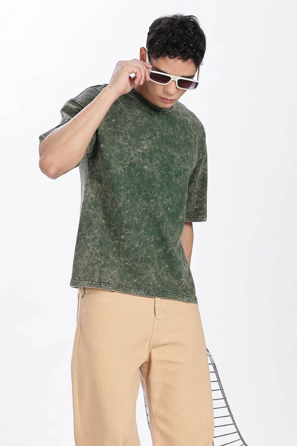 Man wearing a green distressed t-shirt and beige pants on a white background