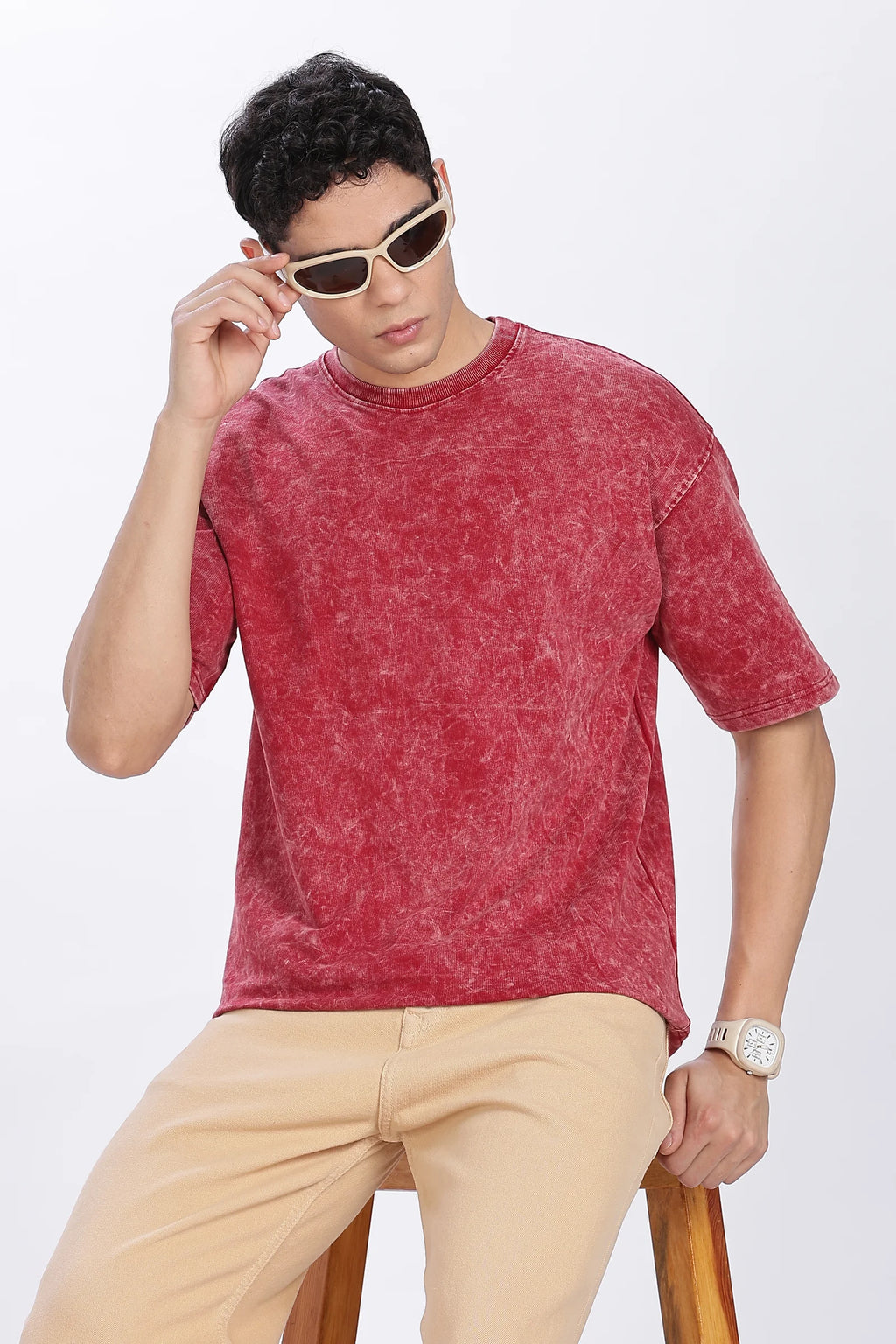 Man wearing a red t-shirt and beige pants with sunglasses on a white background