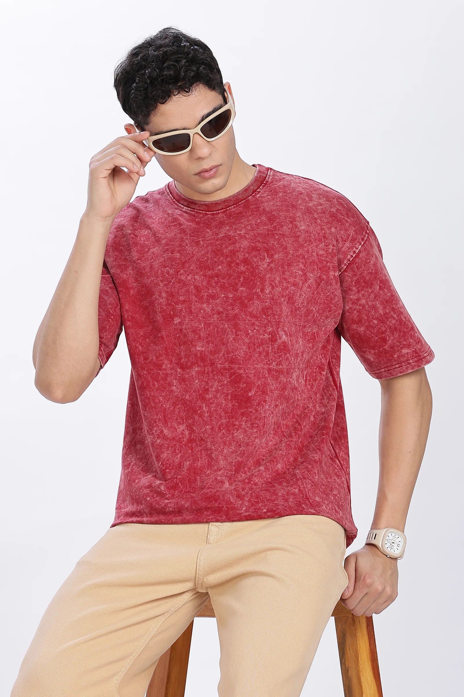 Man wearing a red t-shirt and beige pants with sunglasses on a white background