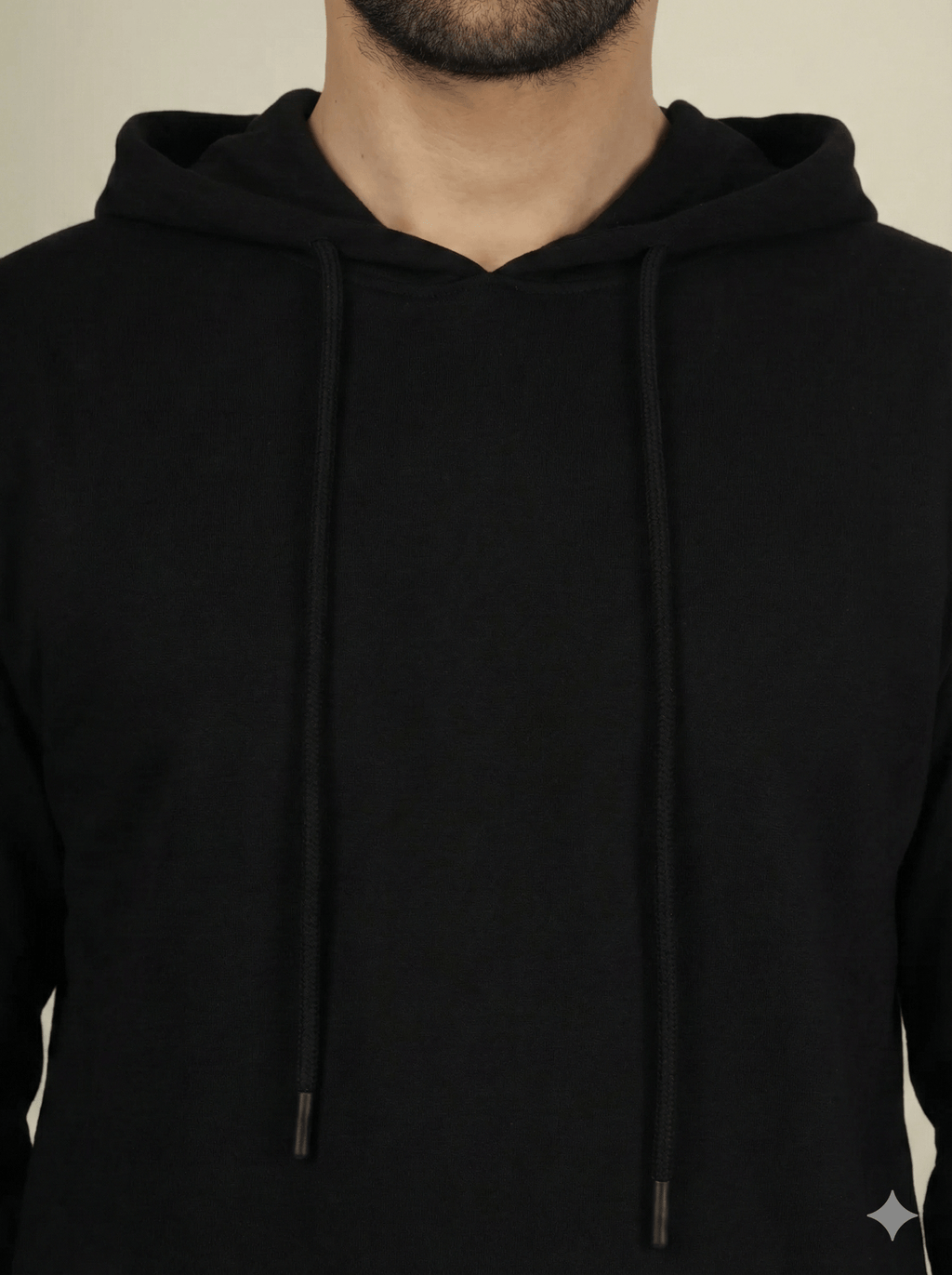 Black hoodie worn by a person on a beige background