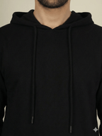 Black hoodie worn by a person on a beige background
