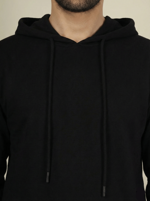 Black hoodie worn by a person on a beige background