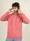 Man wearing a pink hoodie adjusting headphones against a beige background