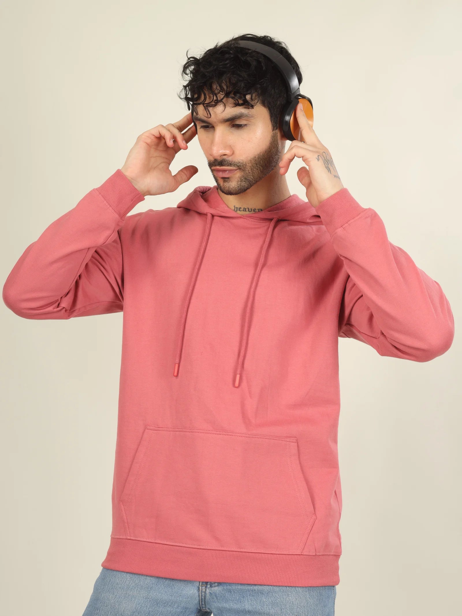 Man wearing a pink hoodie adjusting headphones against a beige background