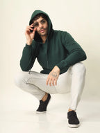 Person wearing a green hoodie and white pants on a plain background
