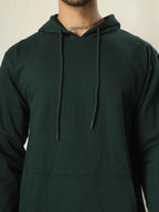 Person wearing a dark green hoodie with a neutral background