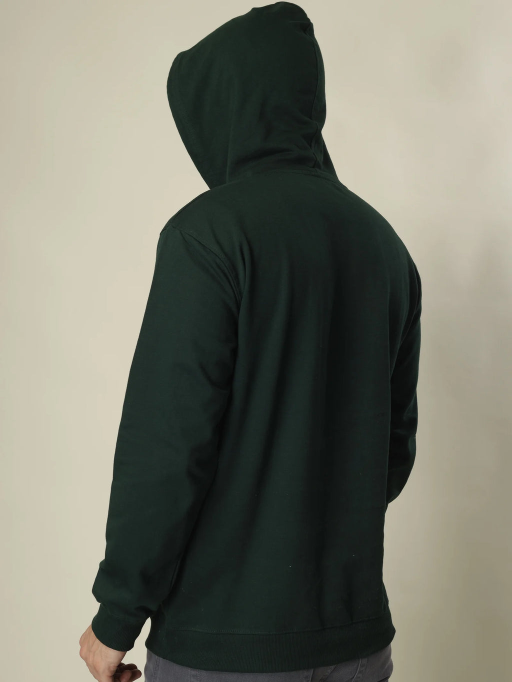 Person wearing a dark green hoodie from behind on a beige background