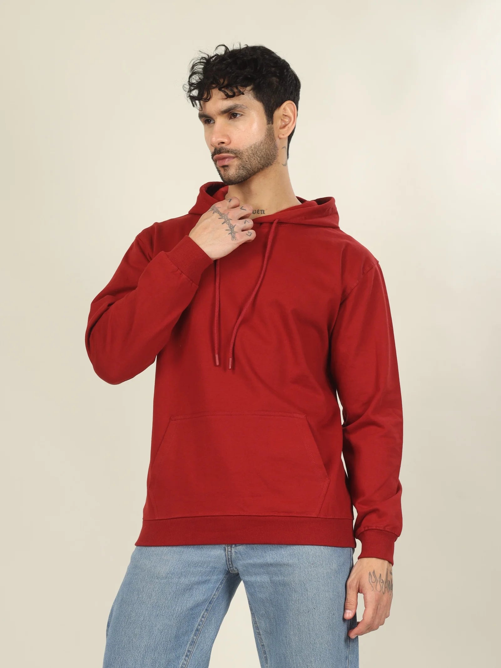 Man wearing a red hoodie and blue jeans against a beige background