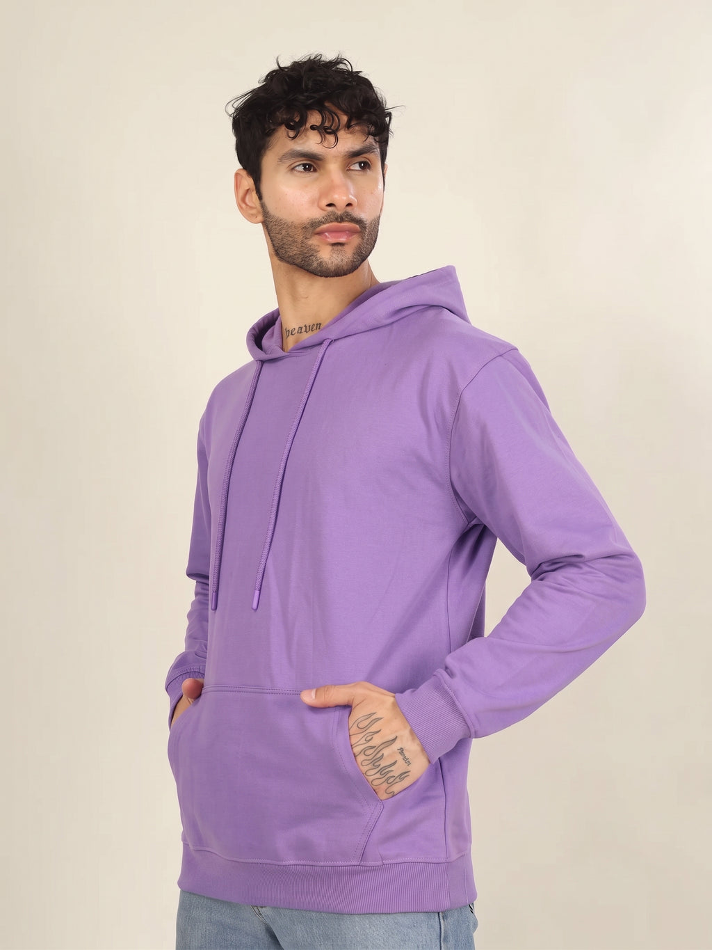 A man wearing a solid purple long-sleeve hoodie with drawstrings and a front kangaroo pocket, standing against a plain beige studio background.