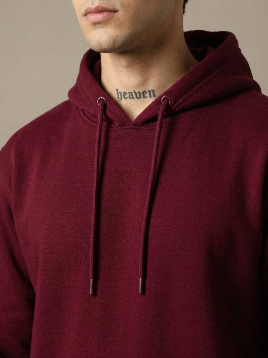 A close-up of a person wearing a burgundy pullover hoodie with matching drawstrings. The person's neck and lower face are visible, and the word 'heaven' is printed in black gothic font inside the collar.