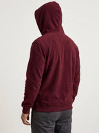 A person shown from the back wearing a maroon hooded sweatshirt and dark gray pants against a plain light background.