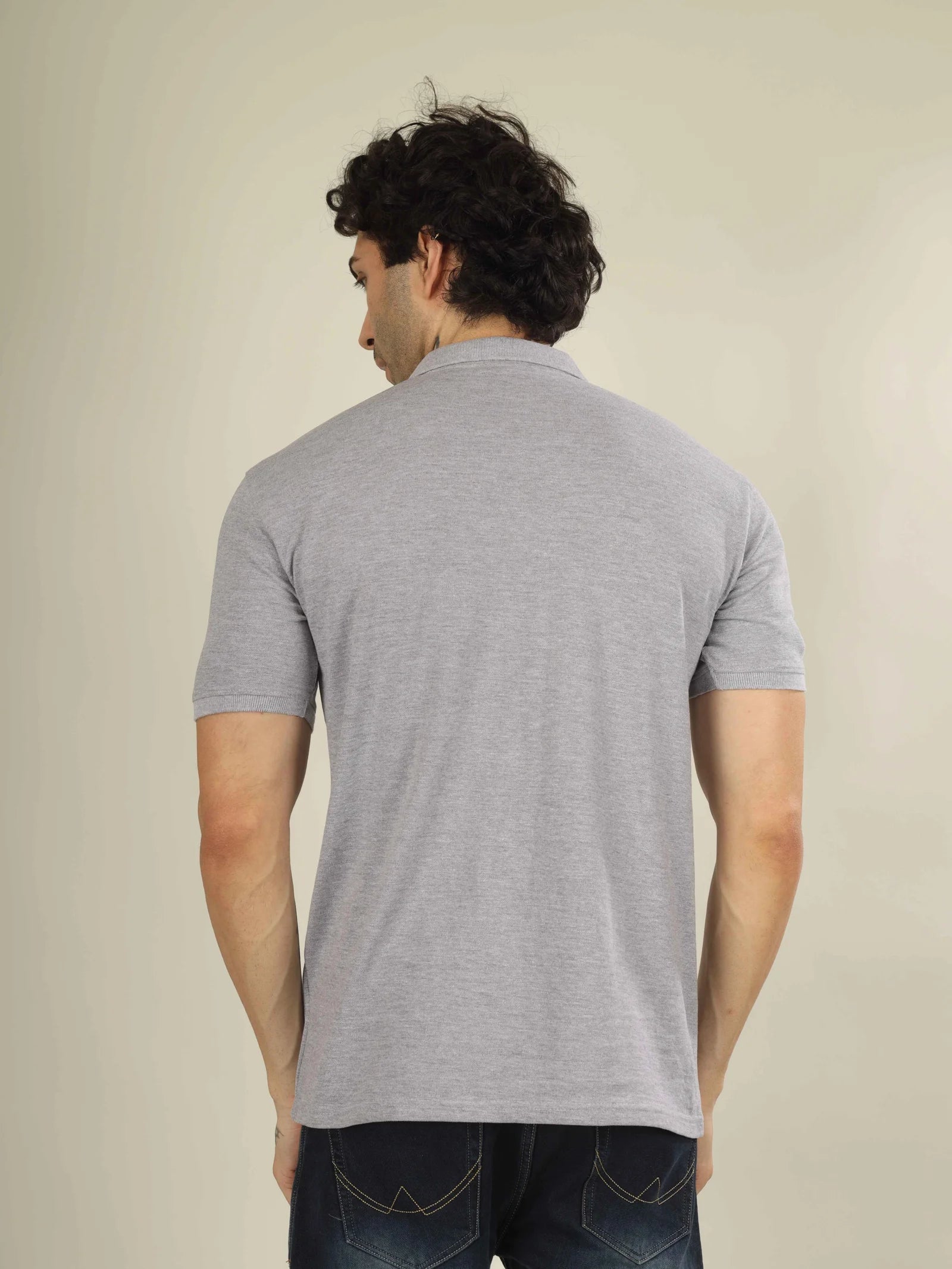 Man wearing a gray polo shirt from behind on a beige background