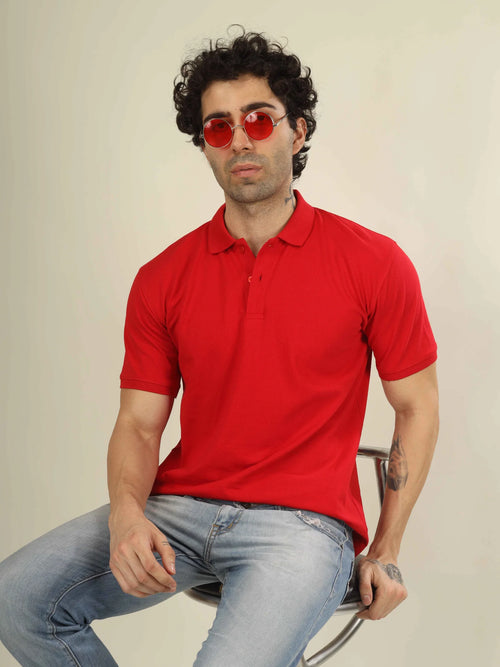 Man wearing a red polo shirt and sunglasses sitting on a chair against a plain background