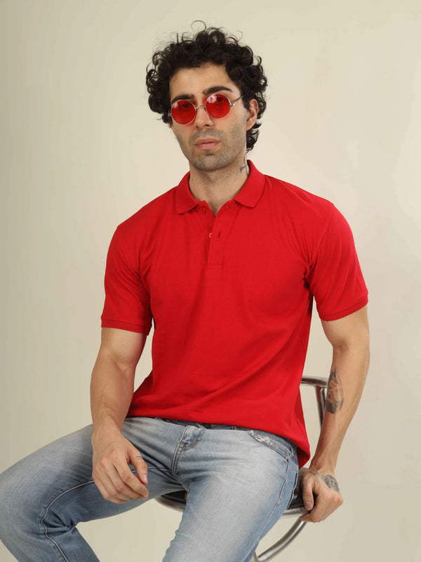 Man wearing a red polo shirt and sunglasses sitting on a chair against a plain background