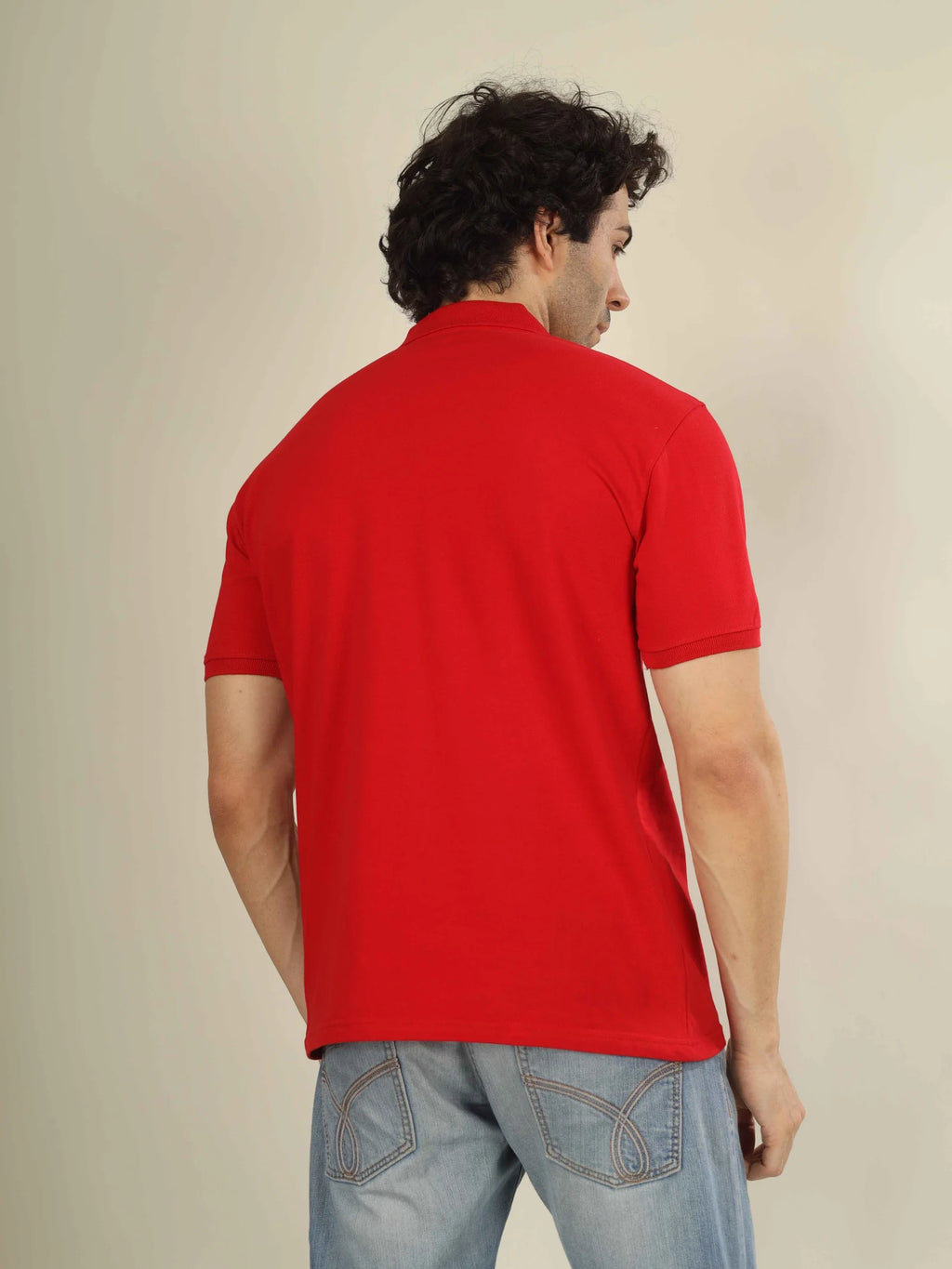 Man wearing a red polo shirt and light blue jeans against a beige background