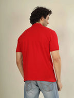 Man wearing a red polo shirt and light blue jeans against a beige background