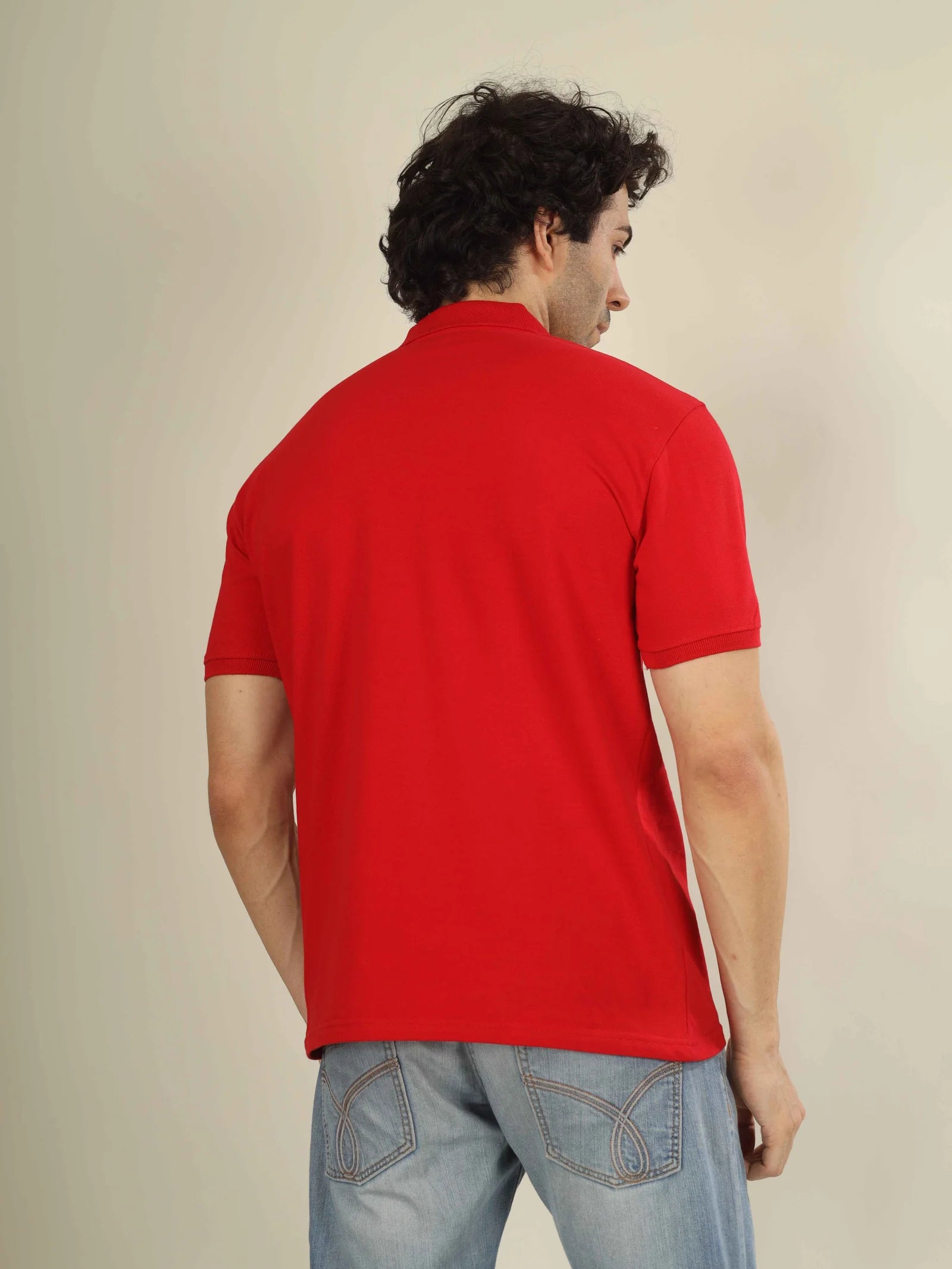 Man wearing a red polo shirt and light blue jeans against a beige background