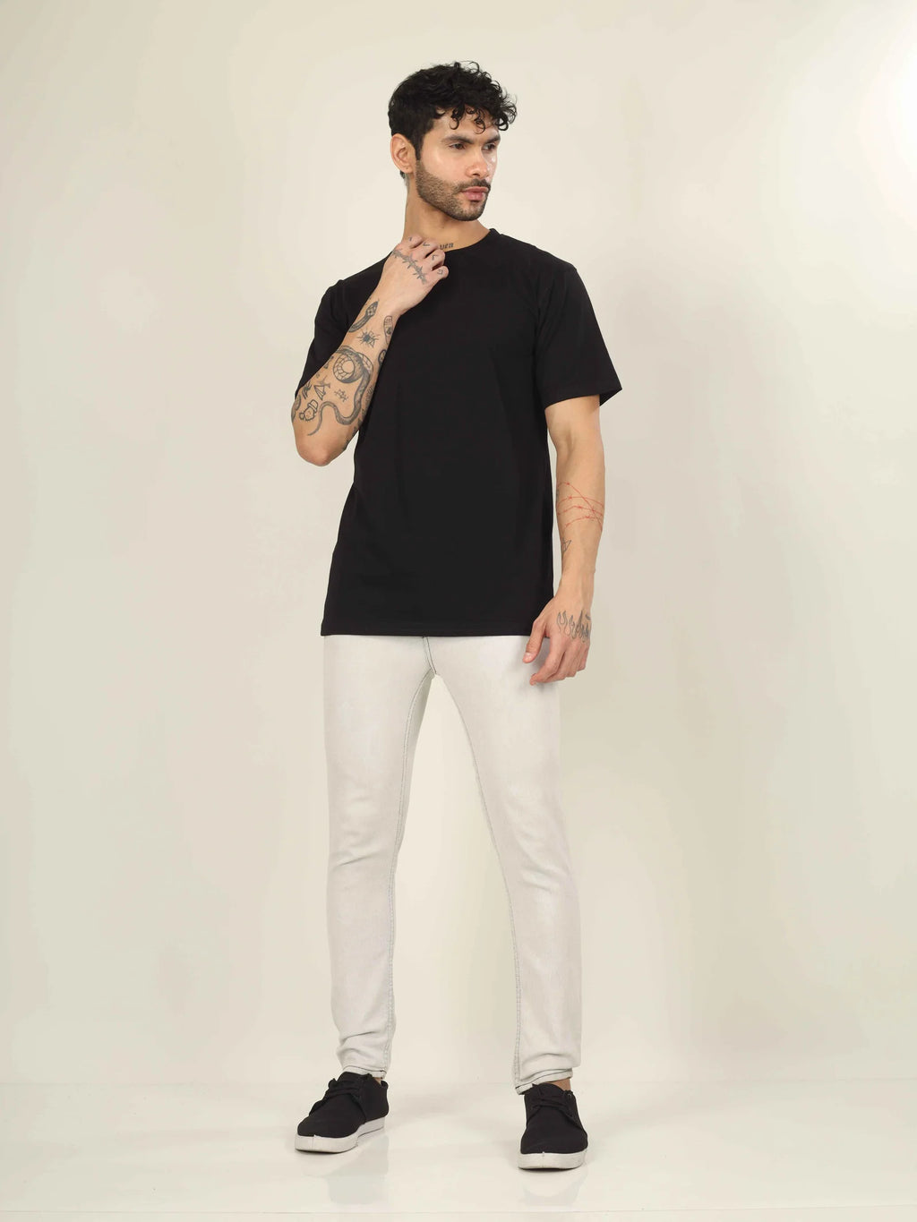 Man wearing a black t-shirt, white pants, and black shoes on a plain background