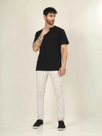 Man wearing a black t-shirt, white pants, and black shoes on a plain background