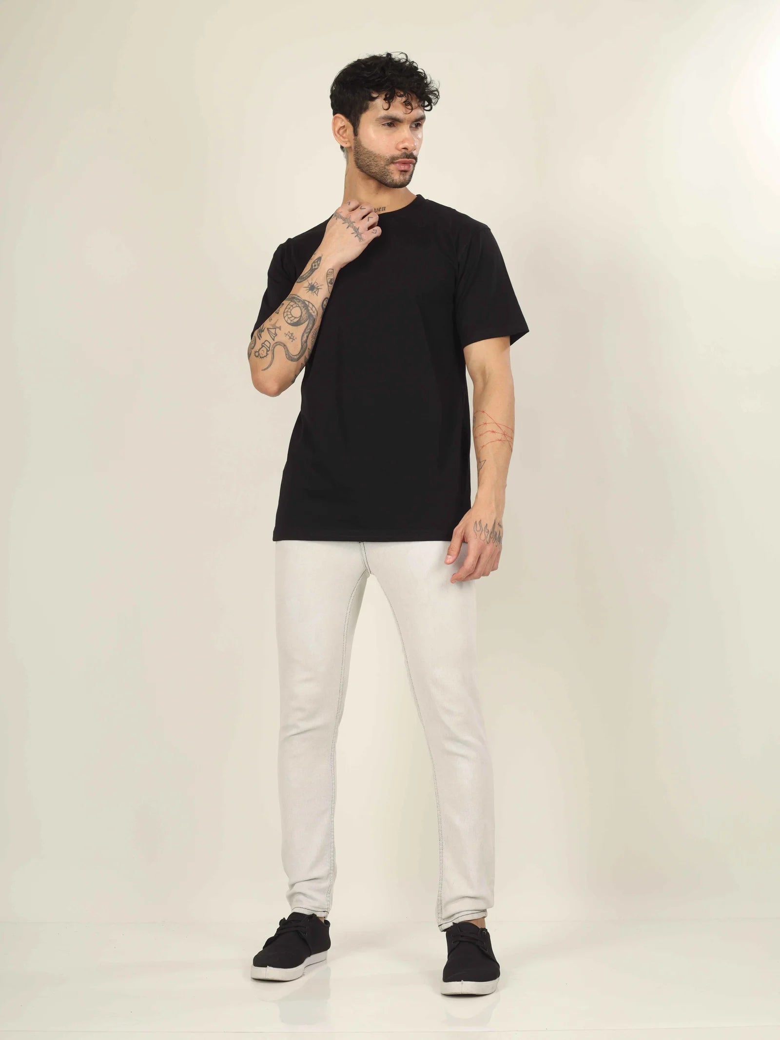 Man wearing a black t-shirt, white pants, and black shoes on a plain background