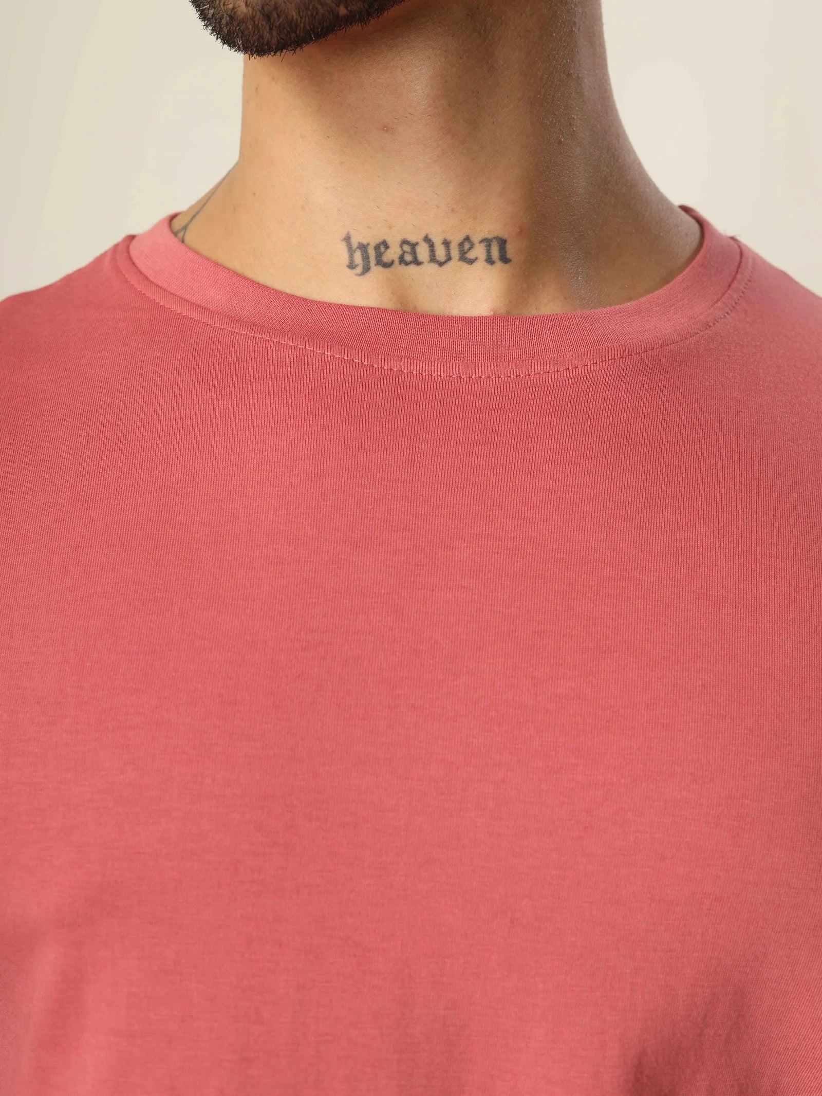 Person wearing a pink shirt with a tattoo on the neck spelling 'heaven'.