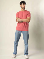 Man wearing a pink t-shirt and blue jeans standing against a plain background