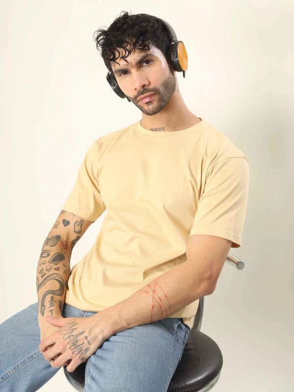 Man wearing a yellow t-shirt and headphones sitting on a chair against a plain background