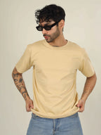 Man wearing a beige t-shirt and sunglasses against a plain background