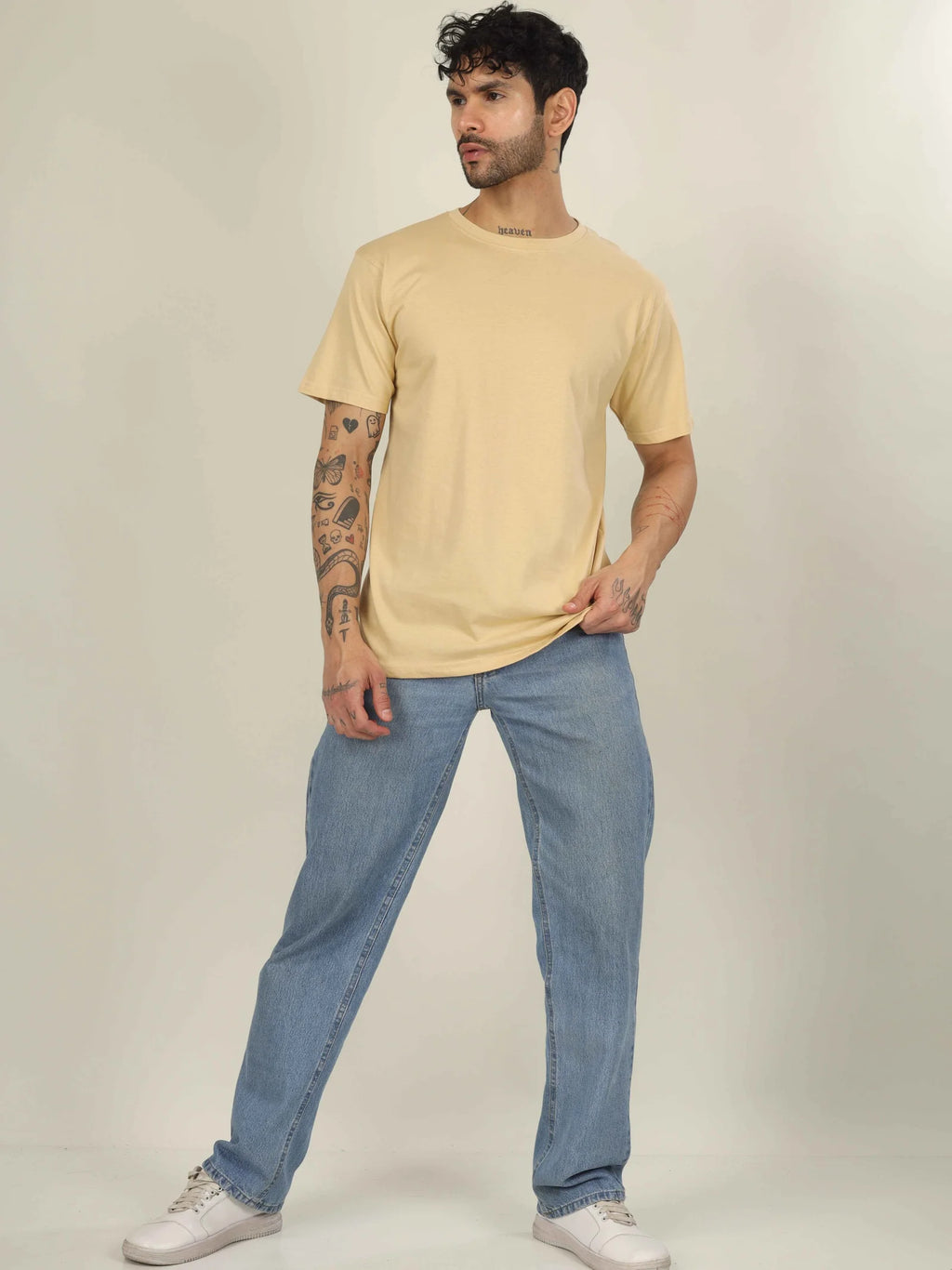 Man wearing a beige t-shirt and blue jeans against a plain background
