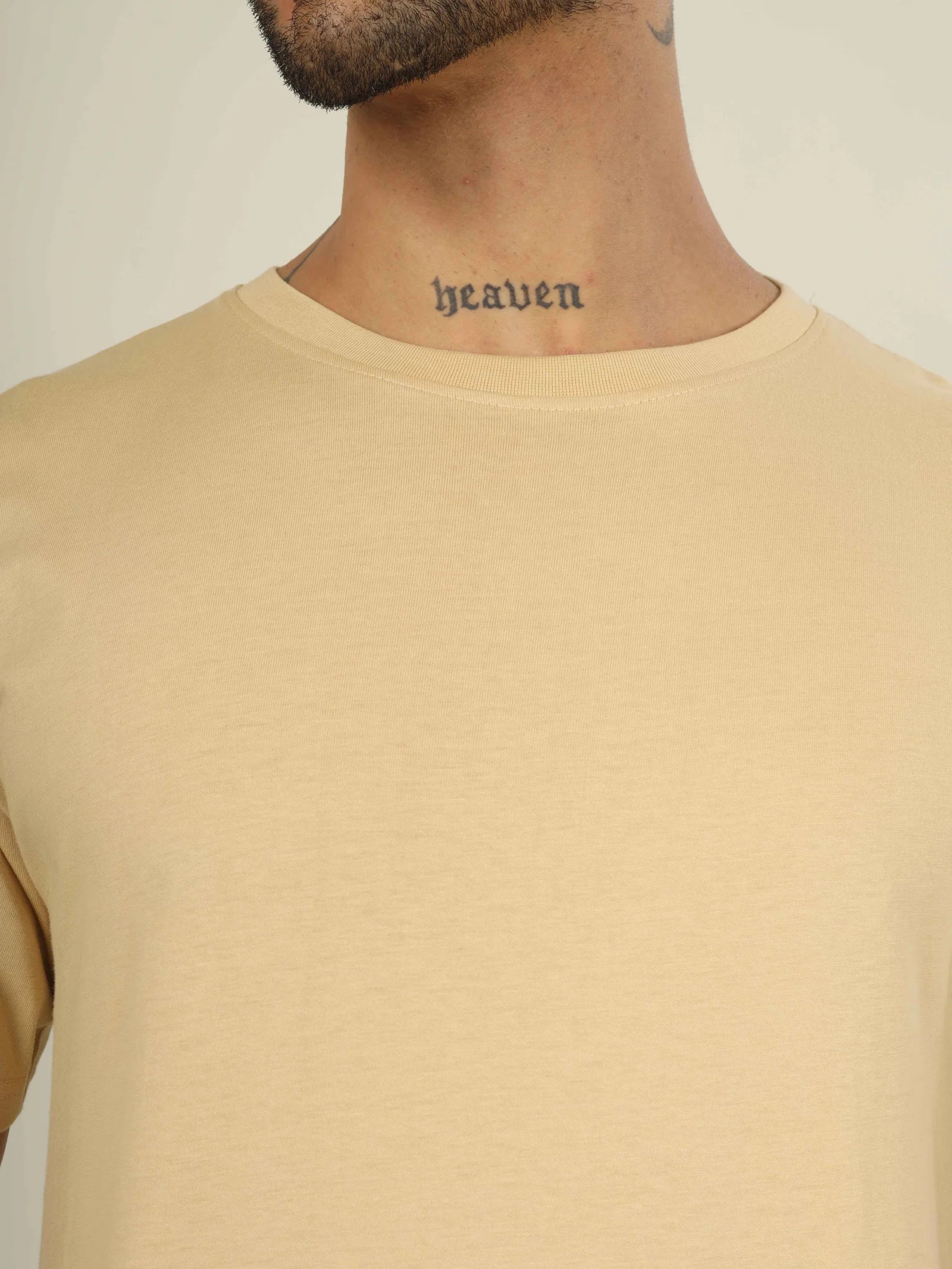 Person wearing a beige t-shirt with a neck tattoo spelling 'heaven' on a plain background