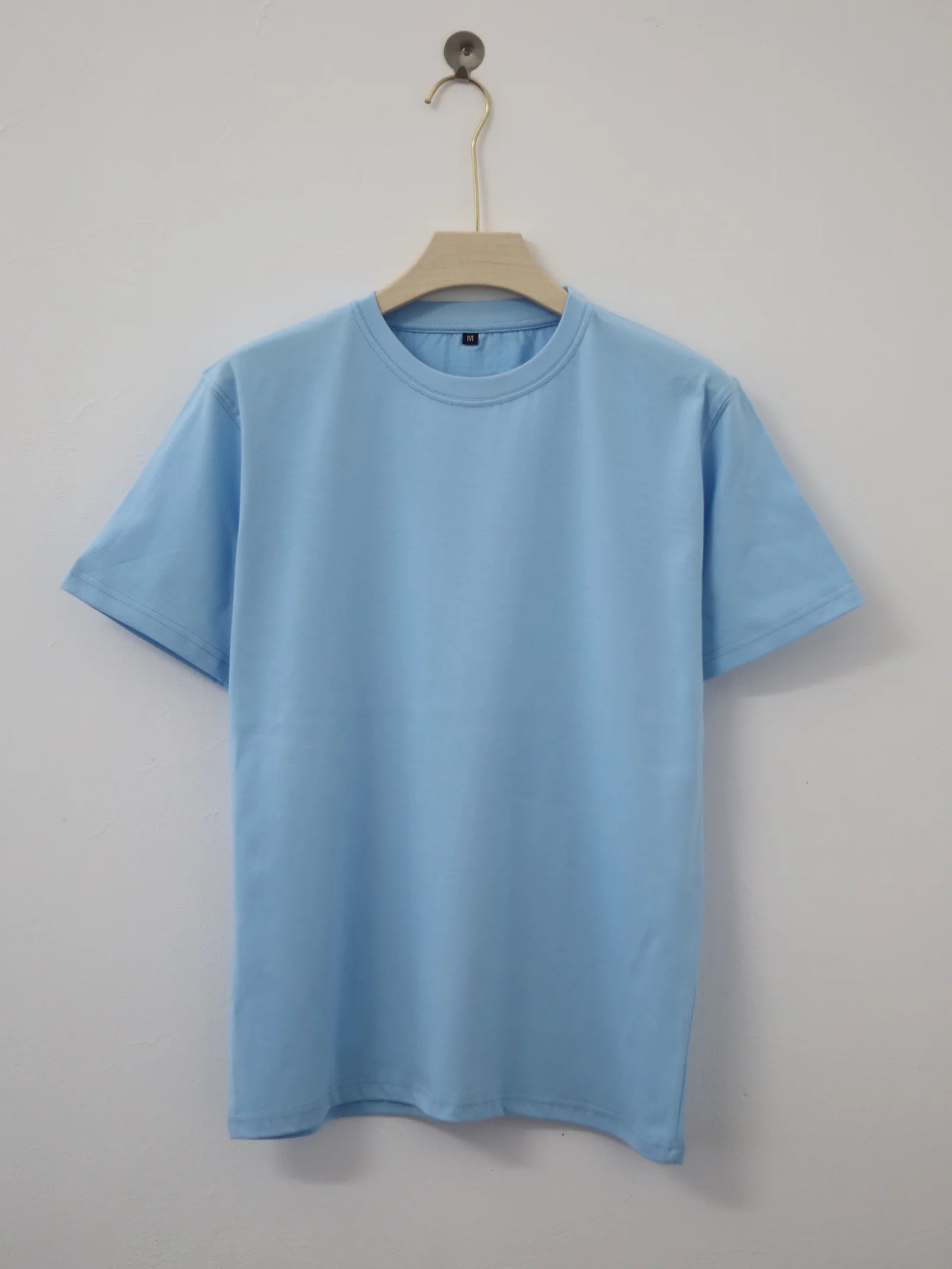 Plain light blue t-shirt on a hanger against a gray background