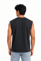 A man viewed from the back wearing a black sleeveless muscle tank top and light blue jeans, standing against a solid white background.