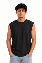 A man wearing a black sleeveless crewneck t-shirt and light blue jeans, standing against a solid white background.