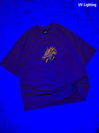 A dark purple t-shirt with a glowing yellow-orange dragon graphic on the chest, displayed under blue UV lighting on a textured blue background. The text 'UV Lighting' is visible in the top right corner.