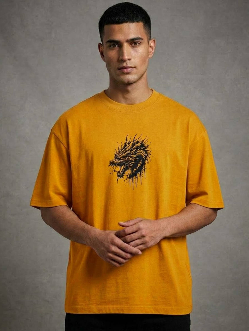 A man wearing a mustard yellow t-shirt with a black distressed dragon graphic on the chest, standing against a textured gray studio background.