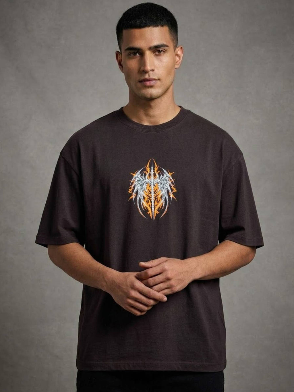 A man wearing a dark brown t-shirt with a graphic of a stylized winged skull in orange, yellow, and white, standing against a textured gray background.