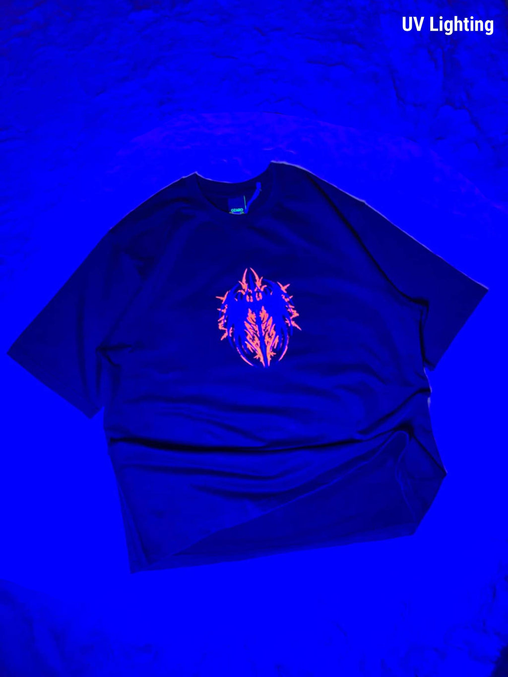 A black t-shirt under UV lighting, showing a glowing neon orange and pink graphic on the chest, with 'UV Lighting' text in the top right corner.