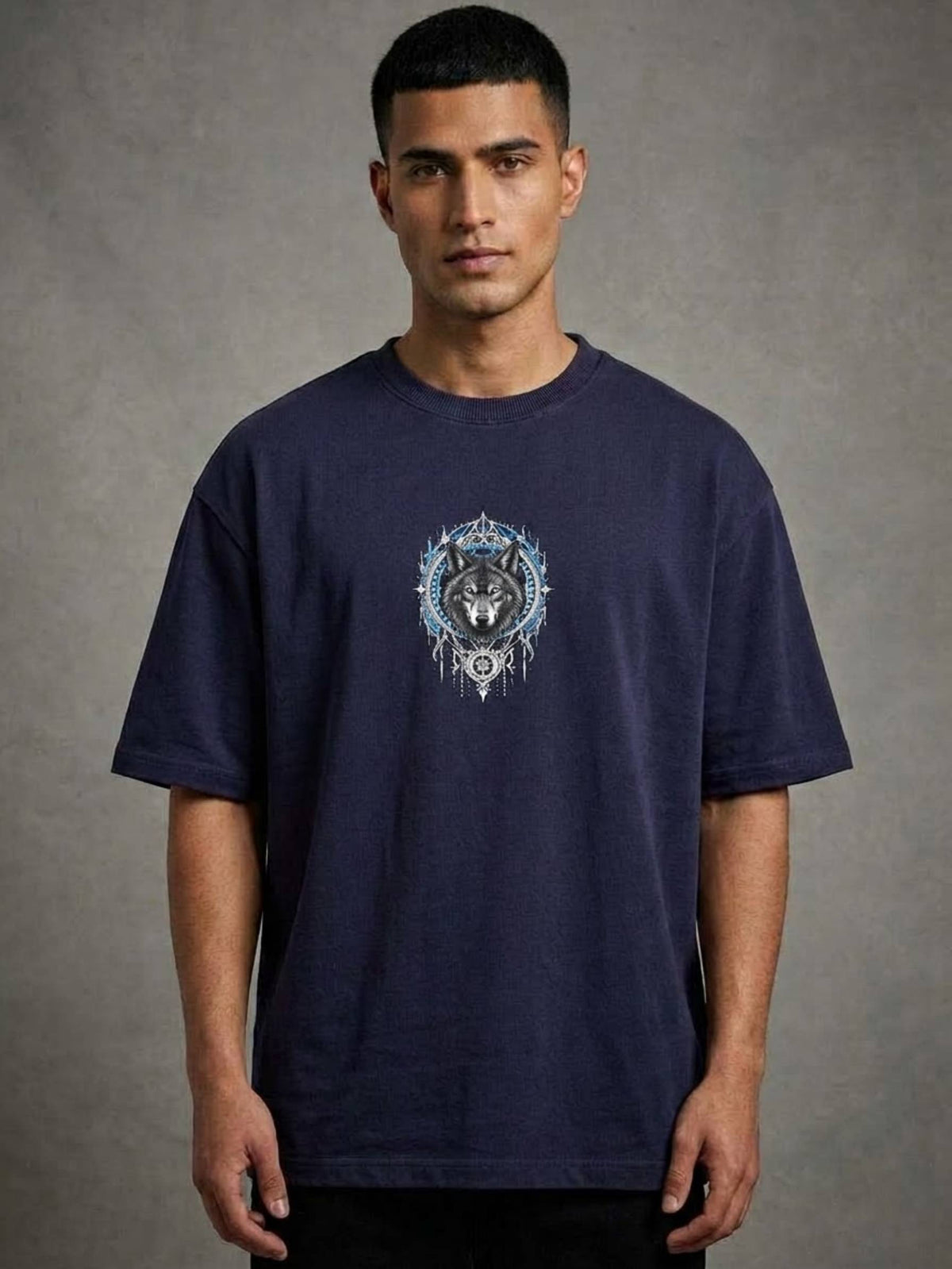 A man wearing a navy blue crewneck t-shirt with a detailed graphic of a wolf inside a circular frame on the chest, set against a textured gray studio background.