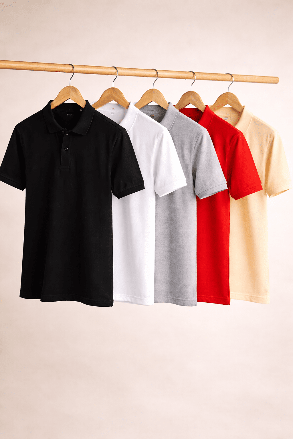 Five polo shirts in black, white, gray, red, and beige hanging on a rack against a beige background.
