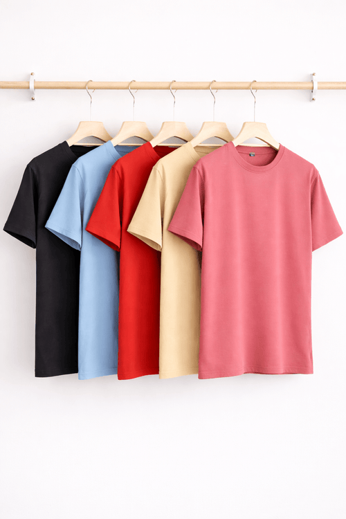 Five plain t-shirts in black, blue, red, beige, and pink hanging on a rack against a white background.